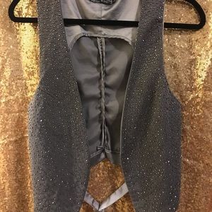Grey vest with metal jeweled embellishment.